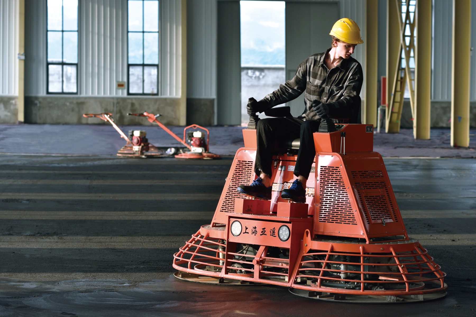 Operator using CONMEC ride-on power trowel on industrial concrete floor